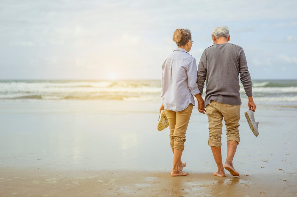 Senior couple walking on the beach holding hands at sunrise - SECURE Act 2.0 updates to retirement savings for 2024