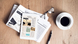 Newspapers and a news tablet on a wooden desk beside coffee—illustrating HFG Trust independence press release
