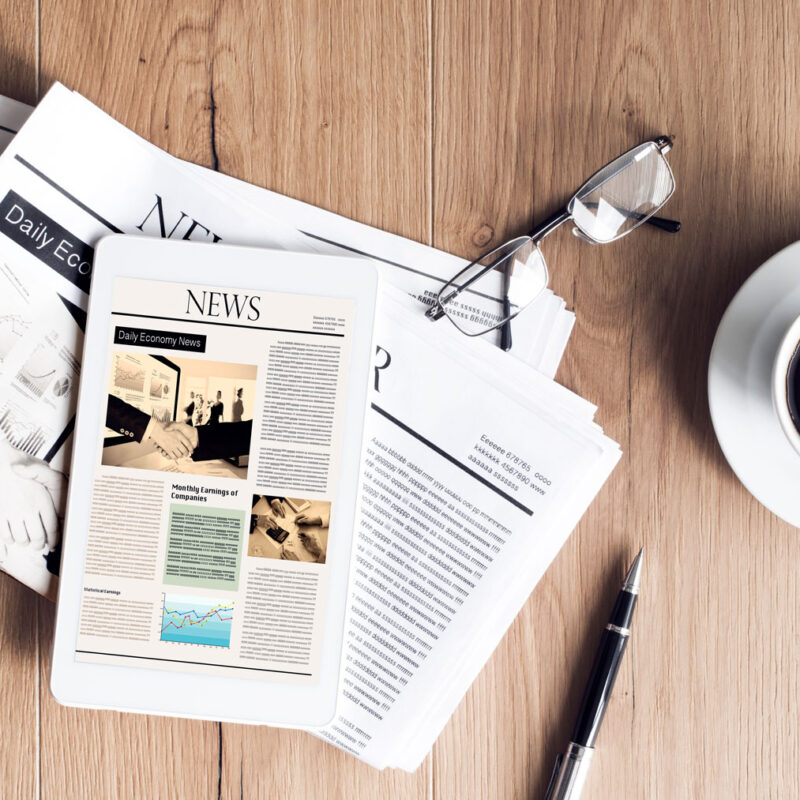 Newspapers and a news tablet on a wooden desk beside coffee—illustrating HFG Trust independence press release