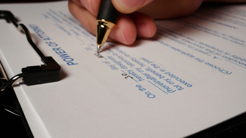 Close-up of hand signing a power of attorney form during estate planning