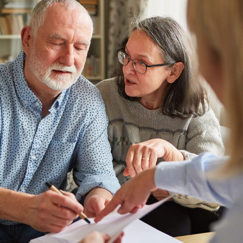Older couple reviewing and signing power of attorney documents with an advisor at home